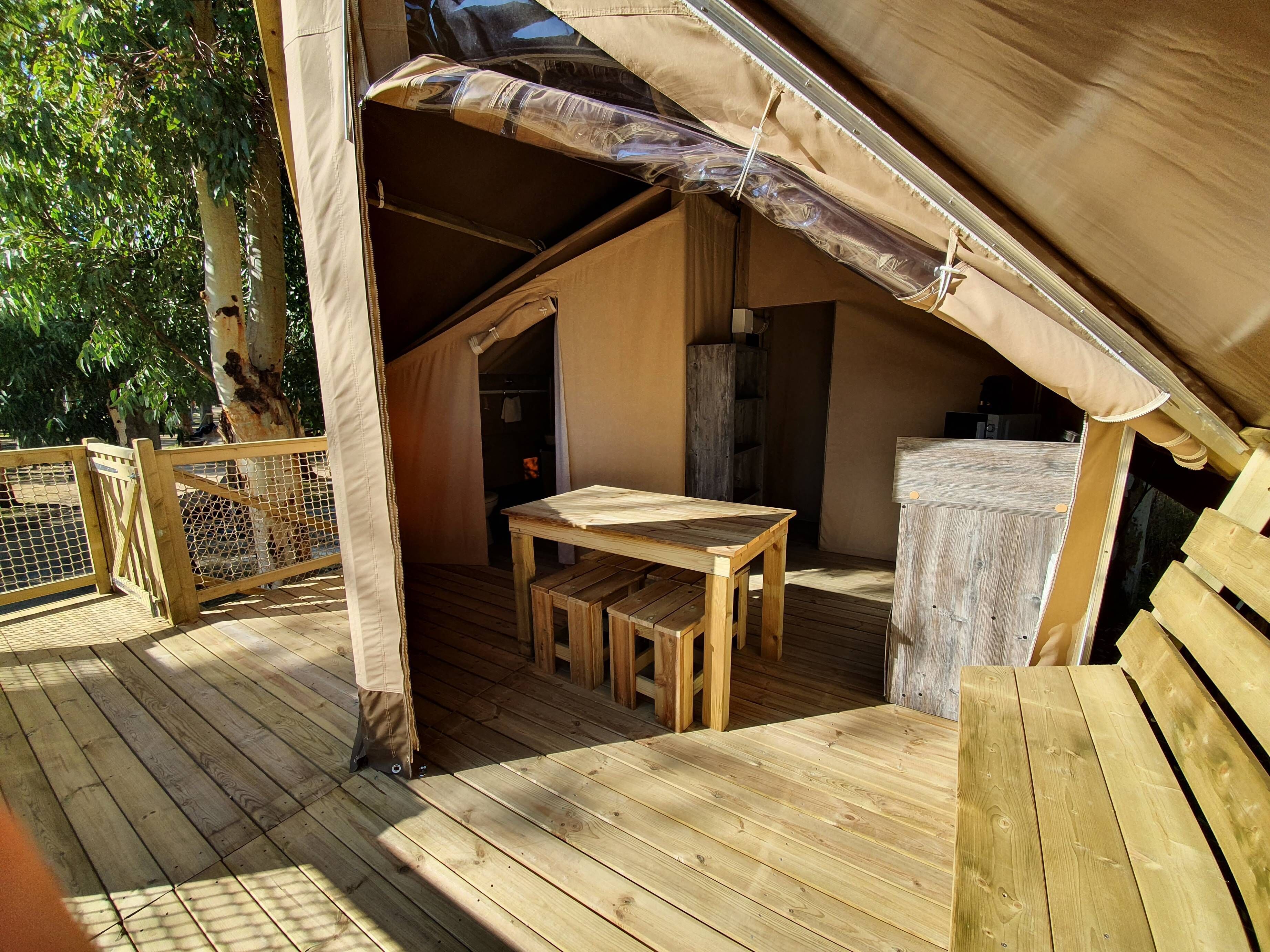 Une terrasse en bois avec une table et des bancs, une structure couverte par une tente et une clôture en bois.