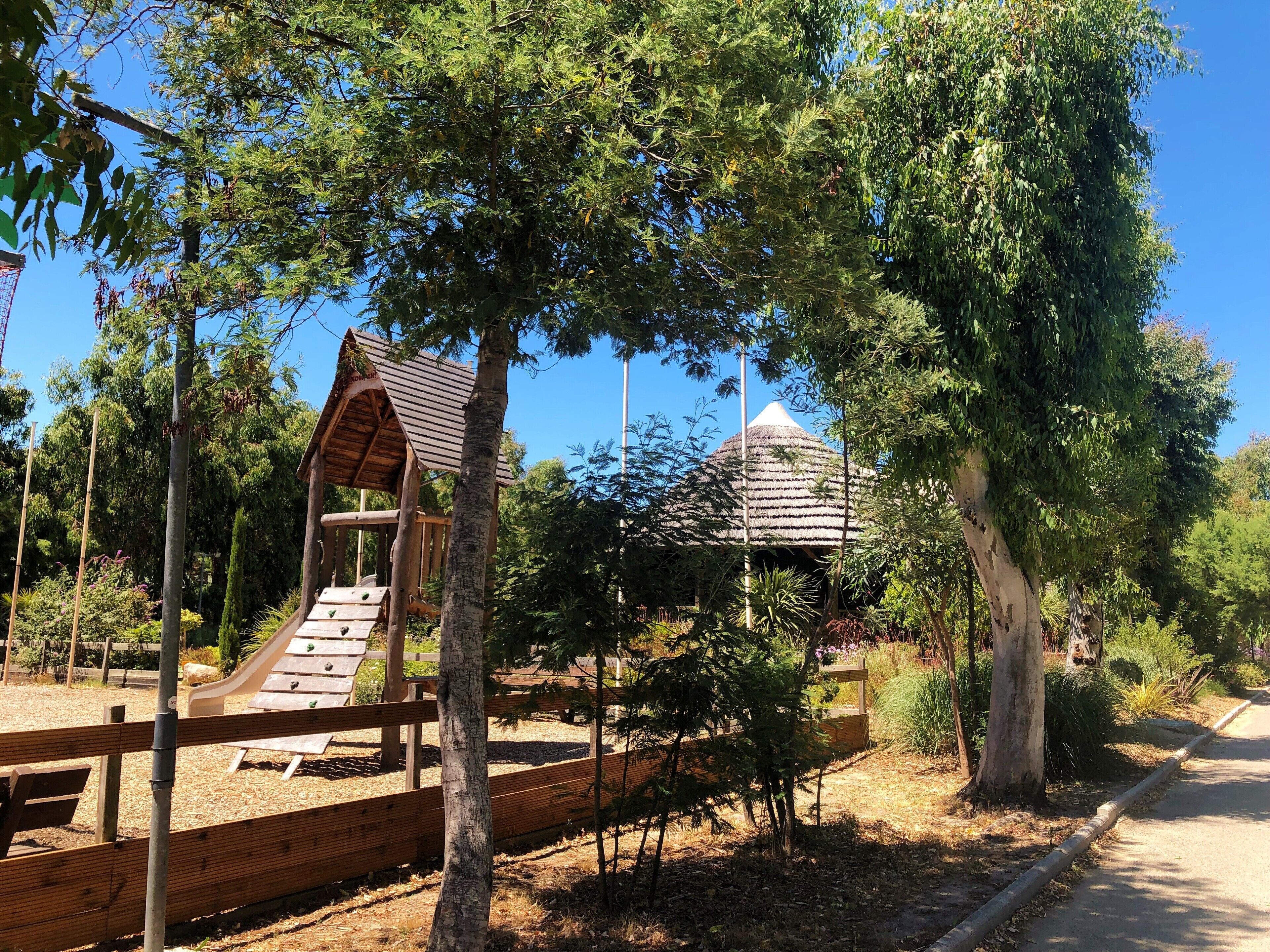 A playground with a slide and climbing structure, surrounded by trees and a clear sky.