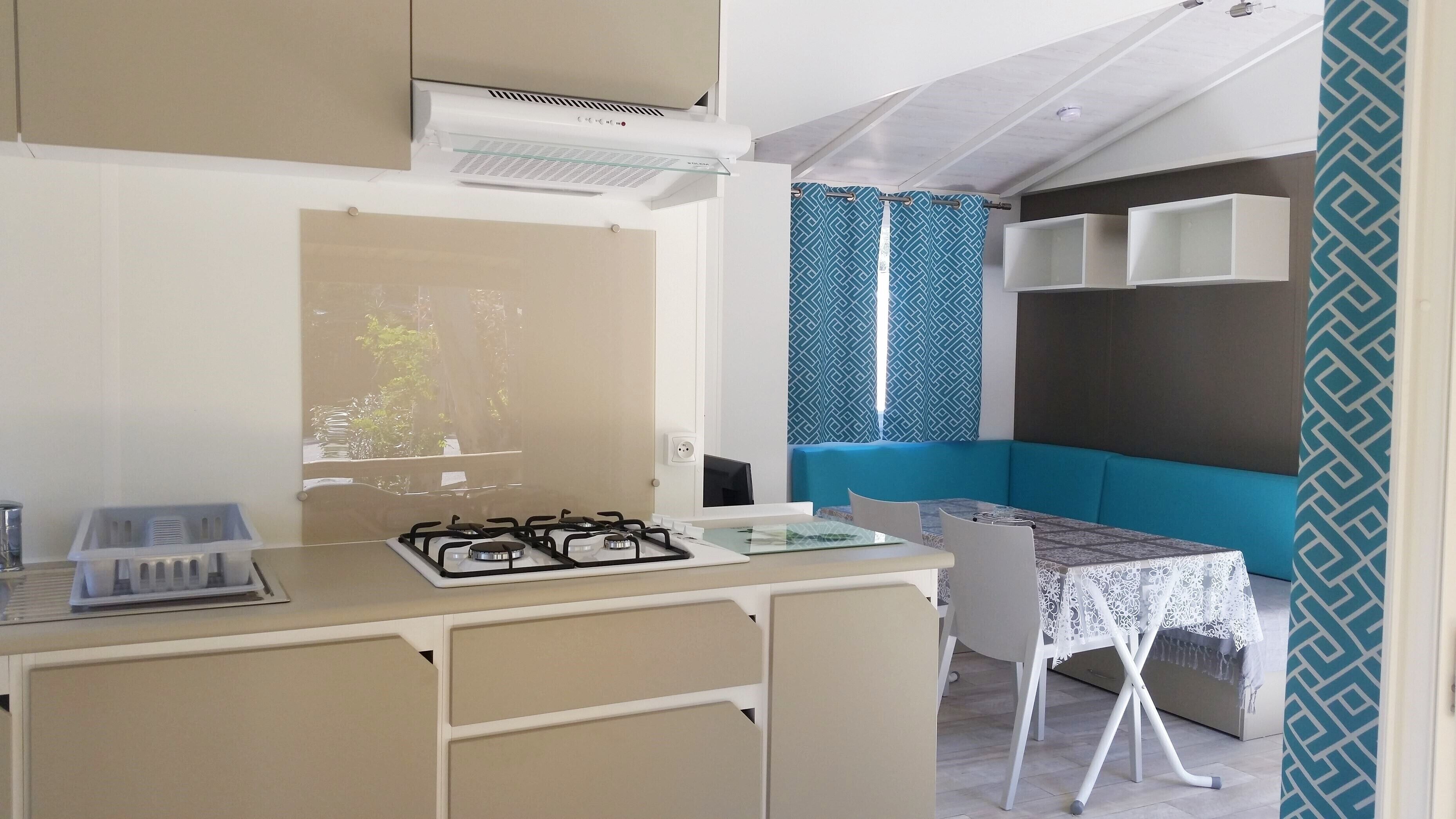Een kleine keuken met een gasfornuis, een eettafeltje en een blauwe met kussens.