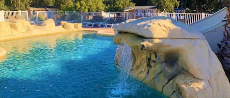 A swimming pool with a rock feature and lounge chairs.