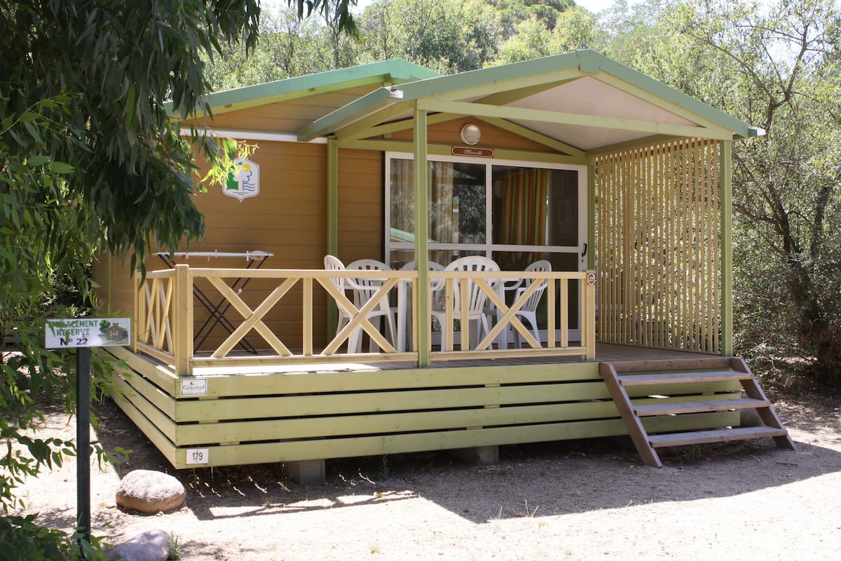 A small wooden cabin with a porch, white plastic chairs, and a sign indicating a reservation number.