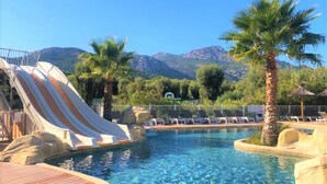 Un área de piscina con tobogán, sillas de descanso y montañas al fondo.