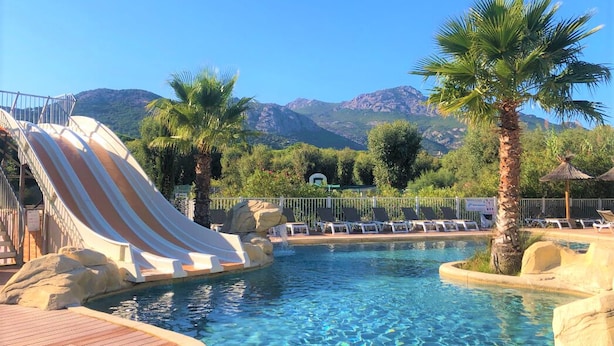 Un área de piscina con tobogán, sillas de descanso y montañas al fondo.