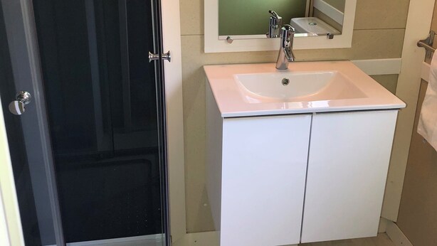 Un baño con mampara de vidrio, un lavamanos blanco con un espejo encima y un inodoro.