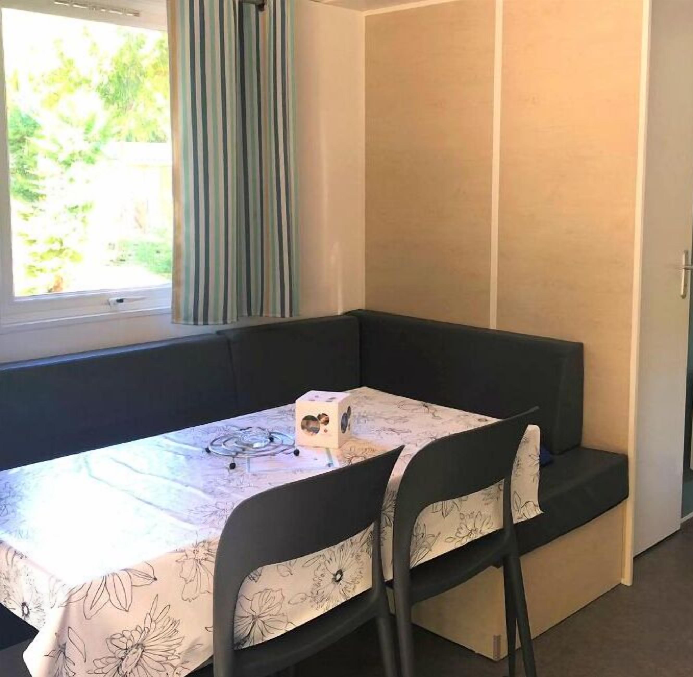Una stanza piccola con un tavolo e due sedie, una finestra con tende e una porta.