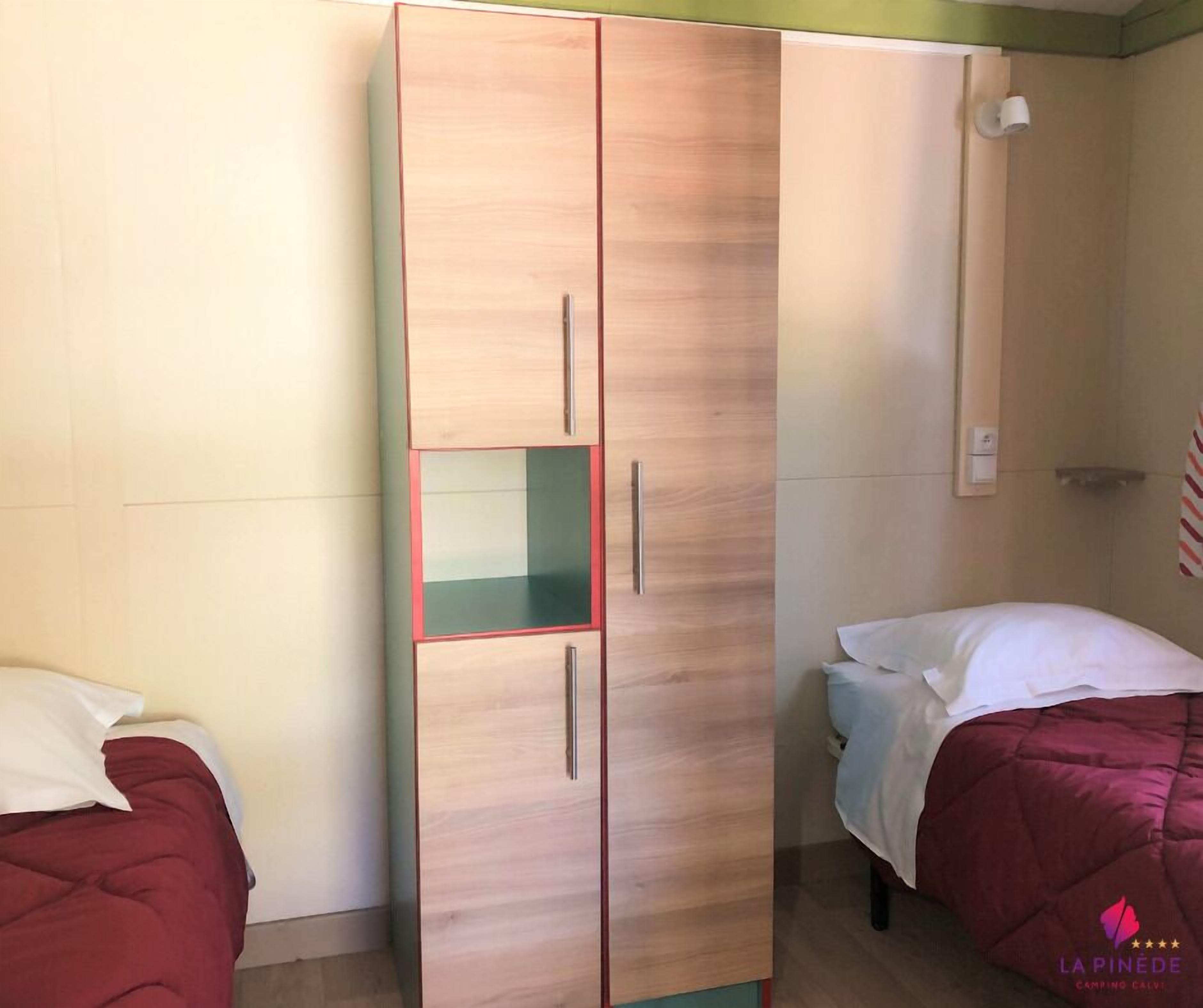 Un dormitorio con un armario grande, dos camas y una mesita pequeña.