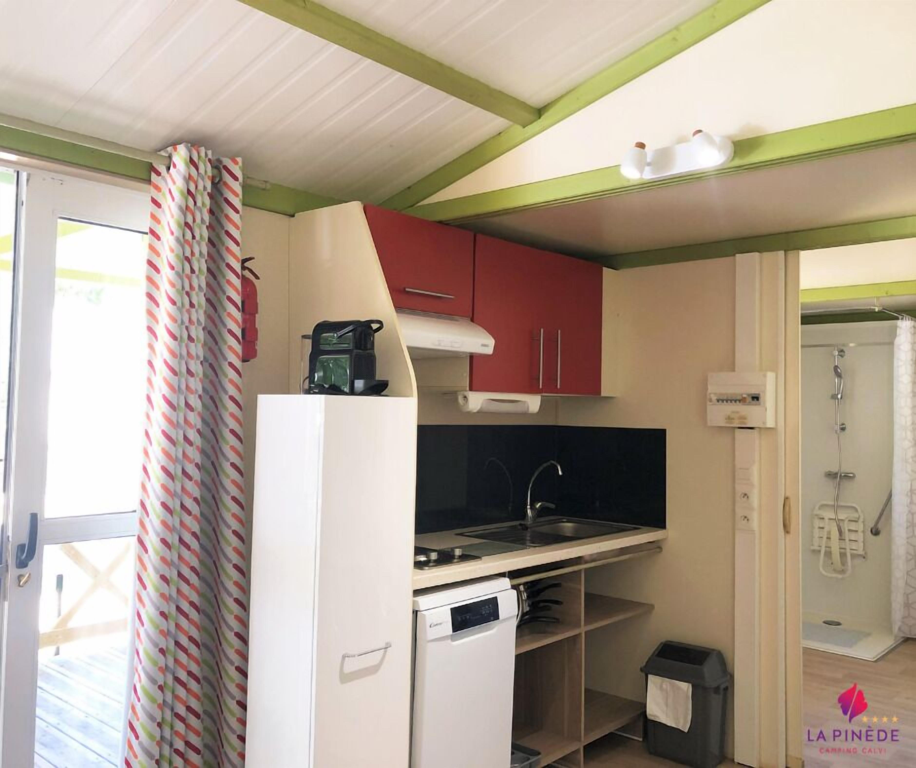 A compact kitchen with a refrigerator, a coffee maker, and a dishwasher. There is a small sink and a shower area visible.