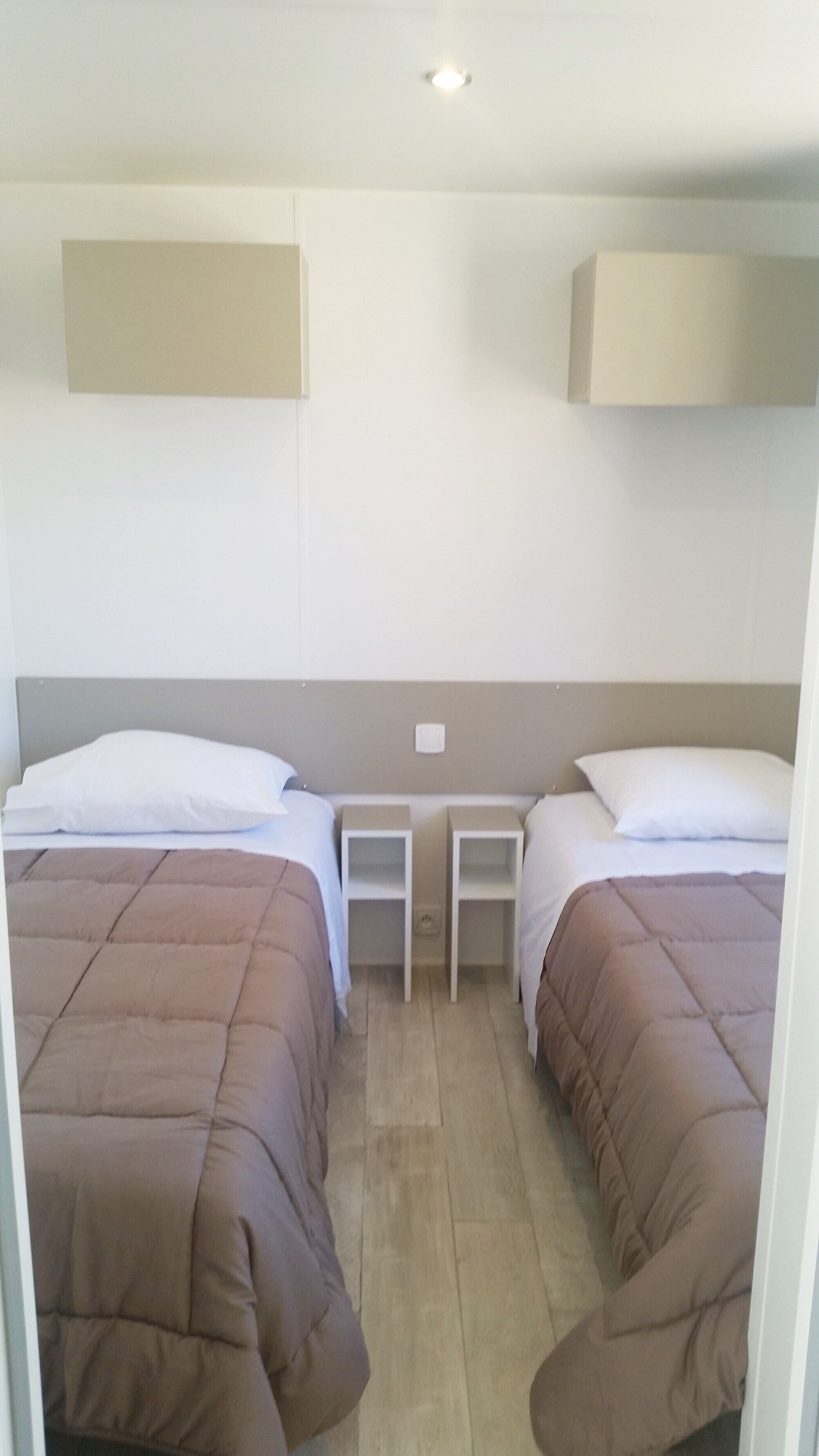Habitación doble con dos camas, cada una con una almohada y una mesita de noche blanca.