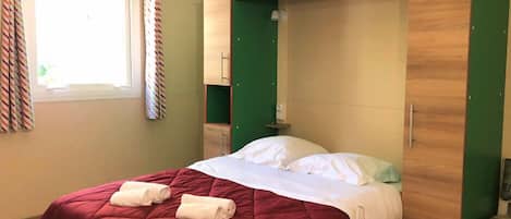 A single bed with a red quilt, a green wall, and a window with curtains.