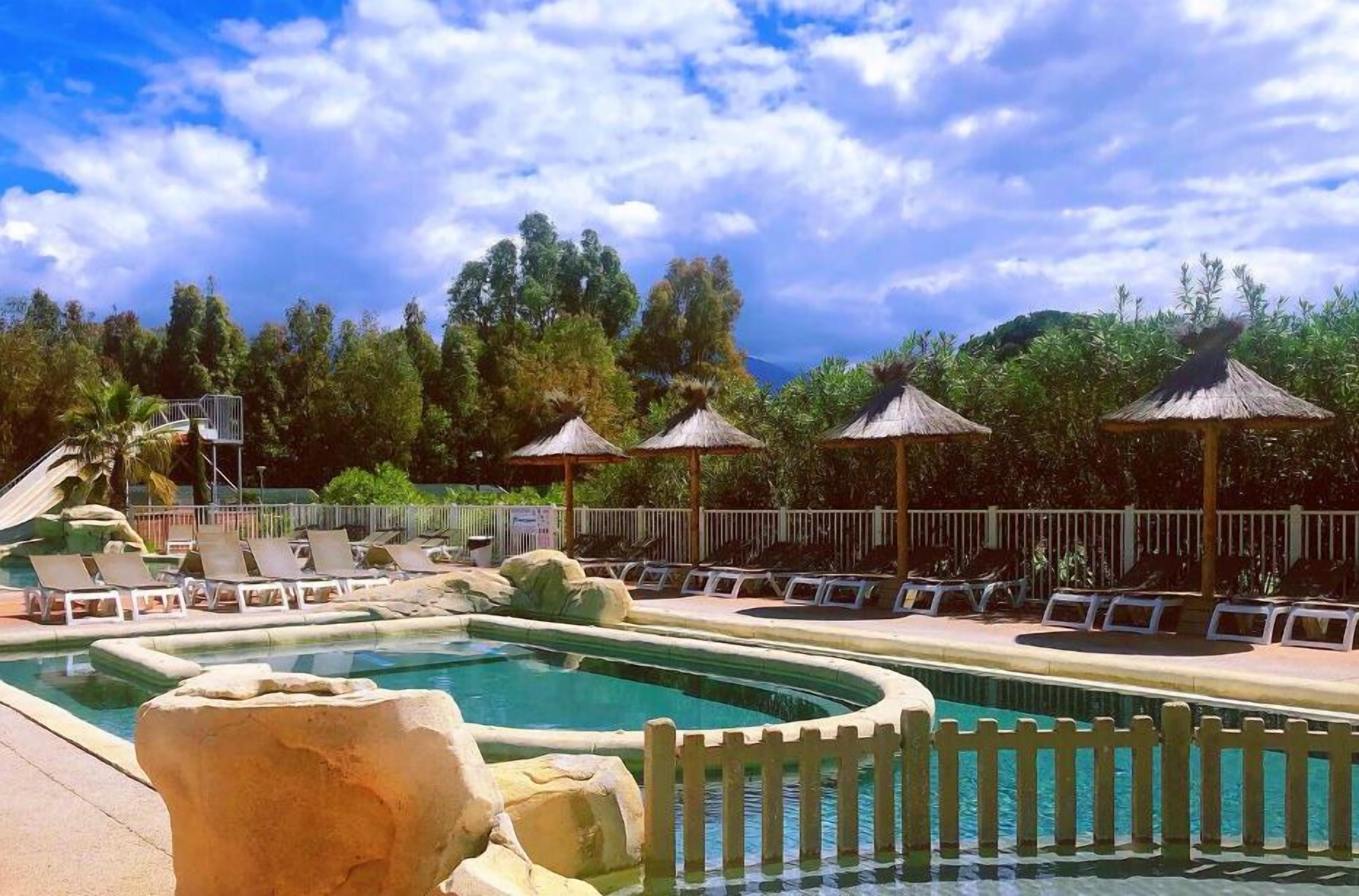 Zona de piscina con sillones de descanso, sombrillas y un entorno natural.