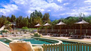 Zona de piscina con sillones de descanso, sombrillas y un entorno natural.
