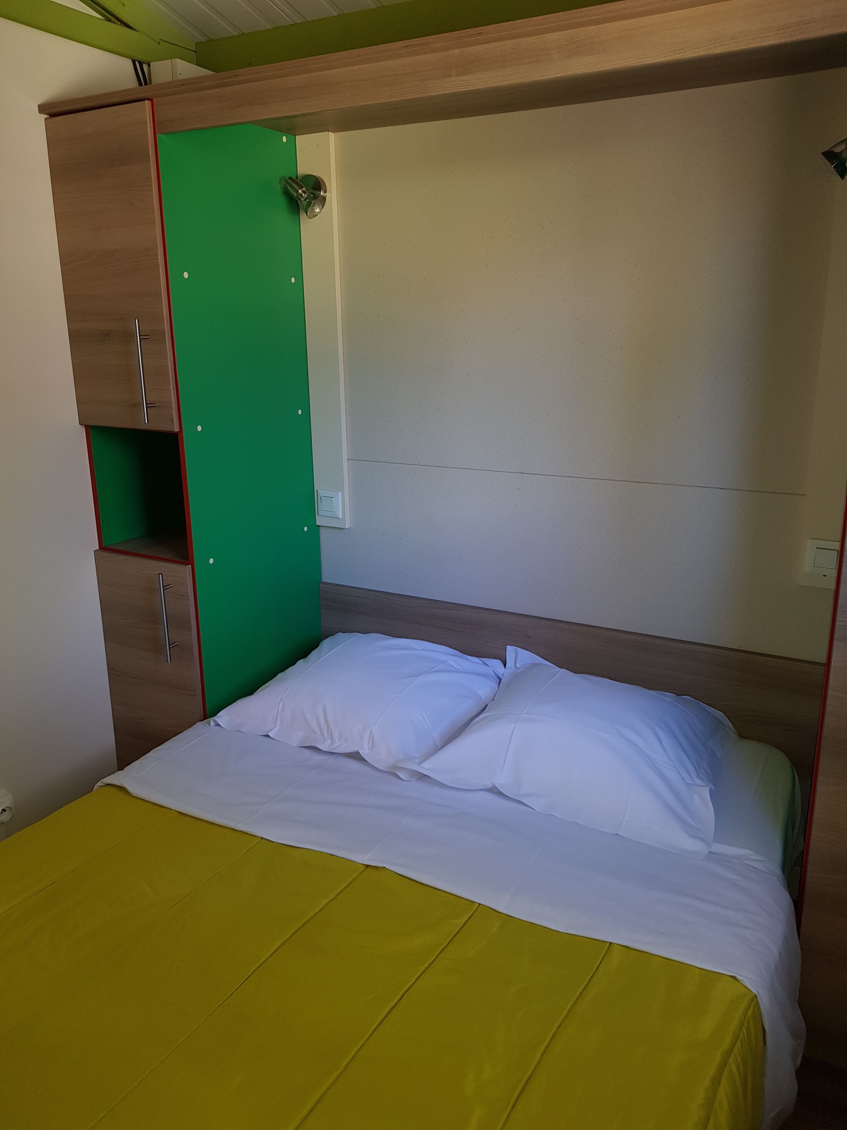 A single bed with white bedding, a green wall panel, and a wooden headboard.