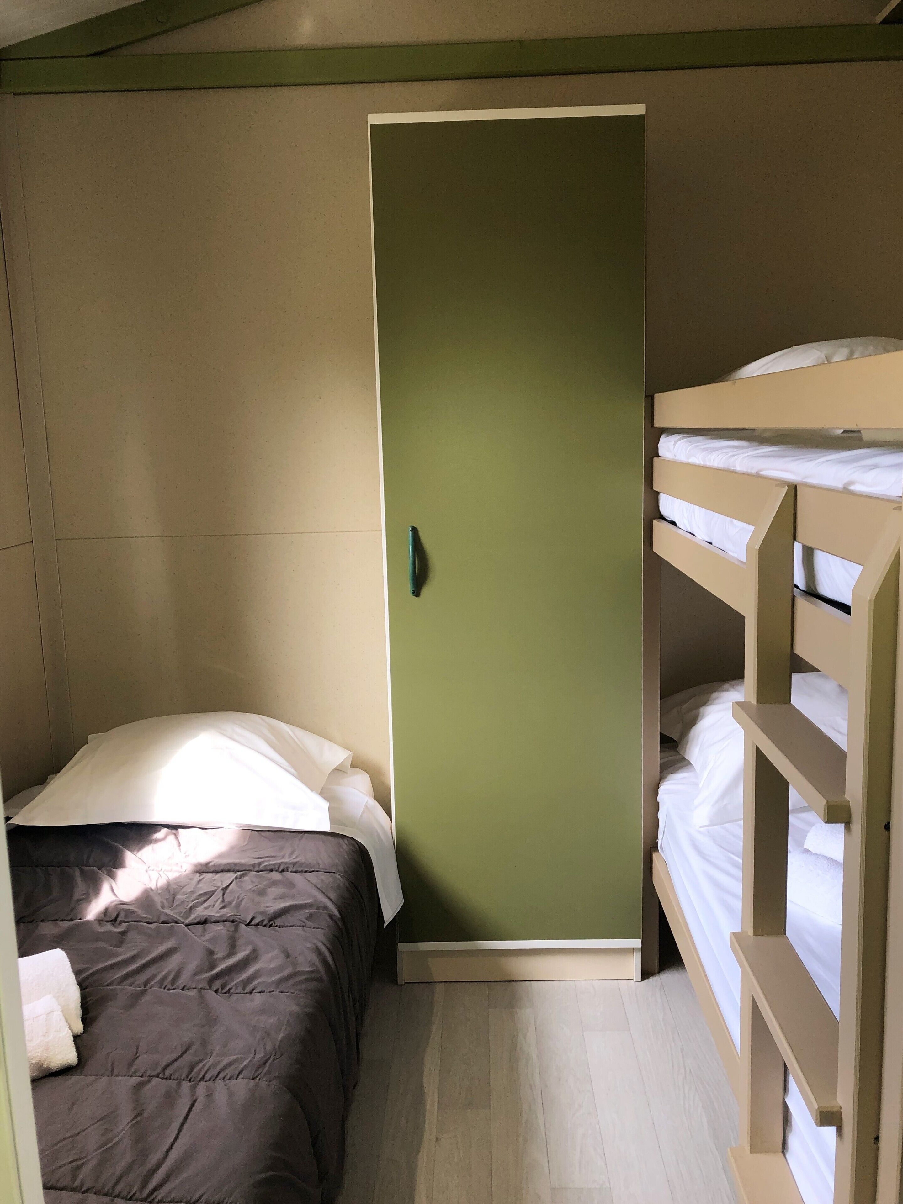 Ein kleines Zimmer mit Etagenbett, einem Einzelbett und einer Tür.