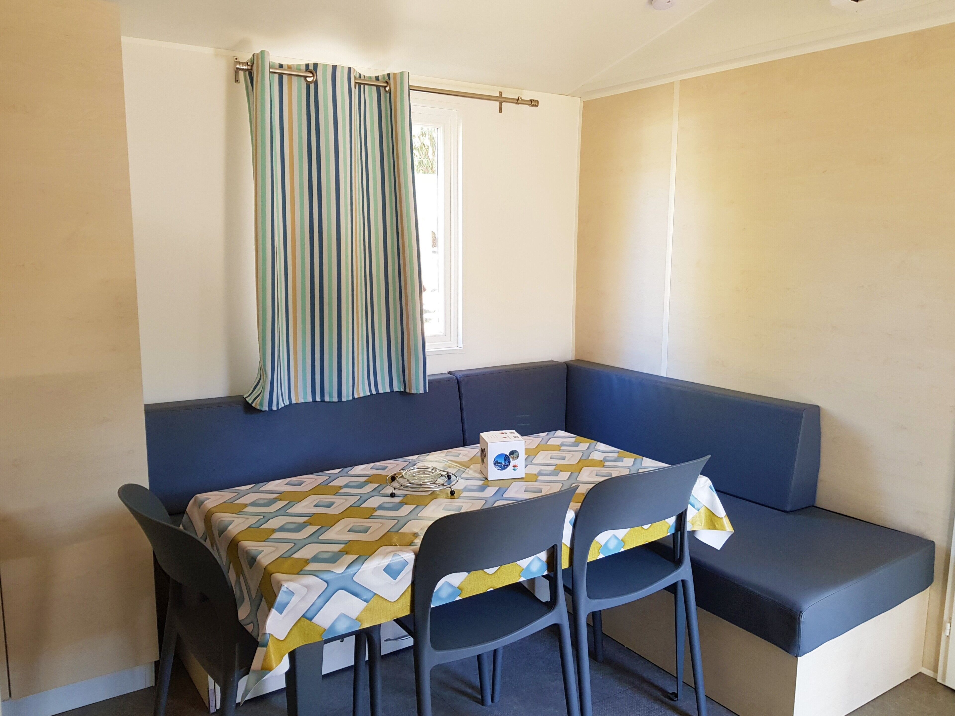 A corner room with a blue sofa, a table with a patterned tablecloth, and a striped curtain.