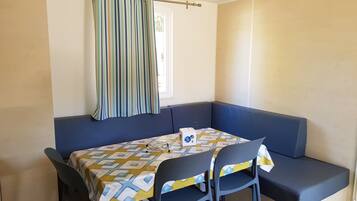 A corner room with a blue sofa, a table with a patterned tablecloth, and a striped curtain.