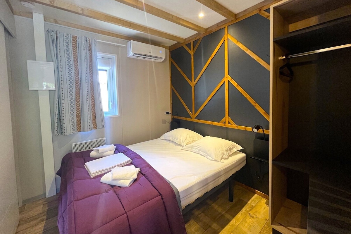 A bedroom with a bed, a window with curtains, an air conditioning unit, and a wooden ceiling structure.