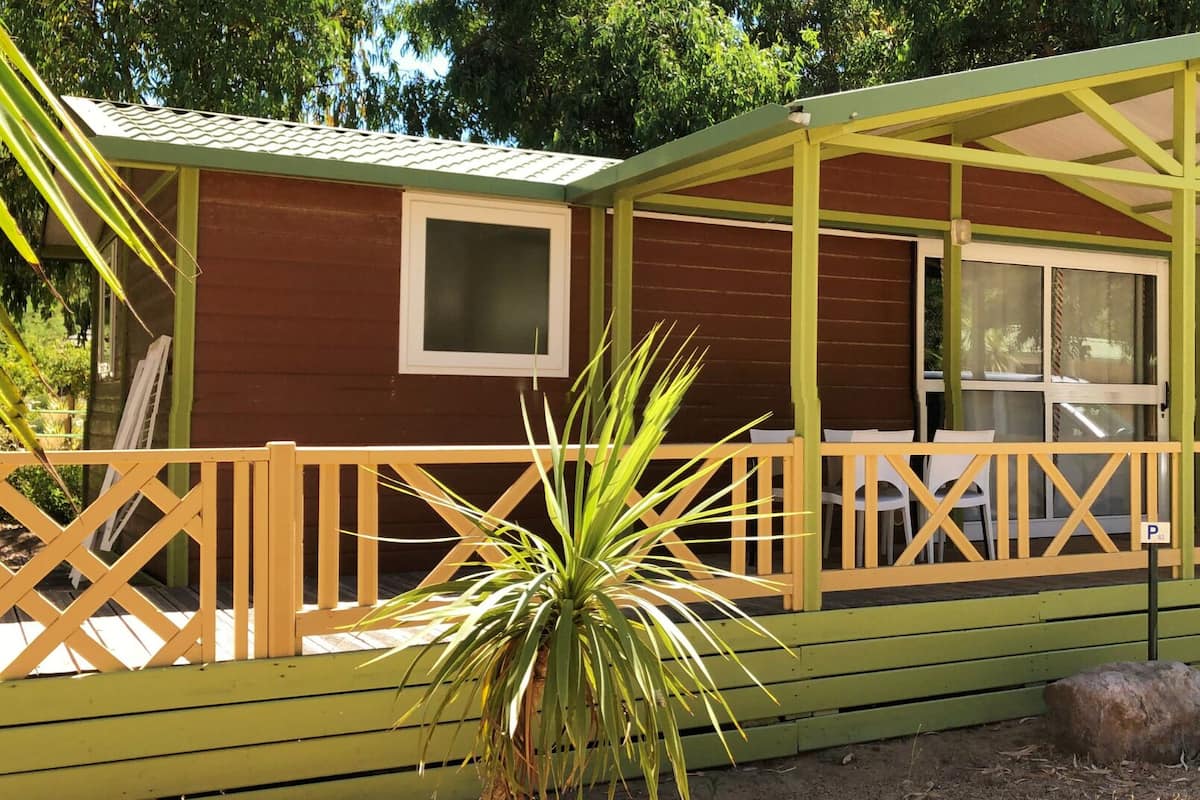 A small, single-story cabin with a green roof and a covered porch.