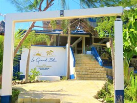 Entrada de un hotel con un letrero que dice "Le Grand Bleu" y una escalera que lleva al edificio.