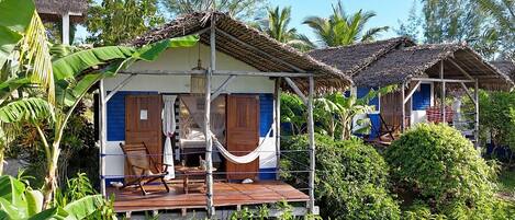 A bungalow with a wooden deck, a hammock, and a thatched roof.