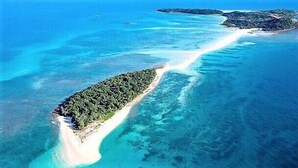 Vista aérea de una isla tropical con aguas turquesas cristalinas, una playa de arena y vegetación densa.