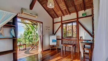 A room with wooden beams, a ceiling fan, a table, chairs, and a view of palm trees.