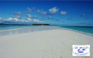 Una playa con arena blanca y agua azul cristalina. Hay un logotipo en la esquina inferior derecha.