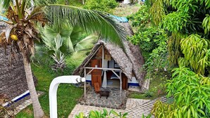 Una cabaña con techo de paja, con un sendero de piedra que la conduce, rodeada de abundante vegetación.