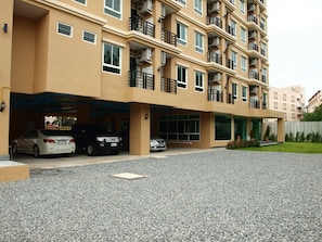 A multi-story residential building with a covered parking area and a gravel driveway.