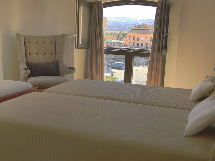 Una habitación de hotel con dos camas, una silla y un ventanal con vistas a edificios y montañas.