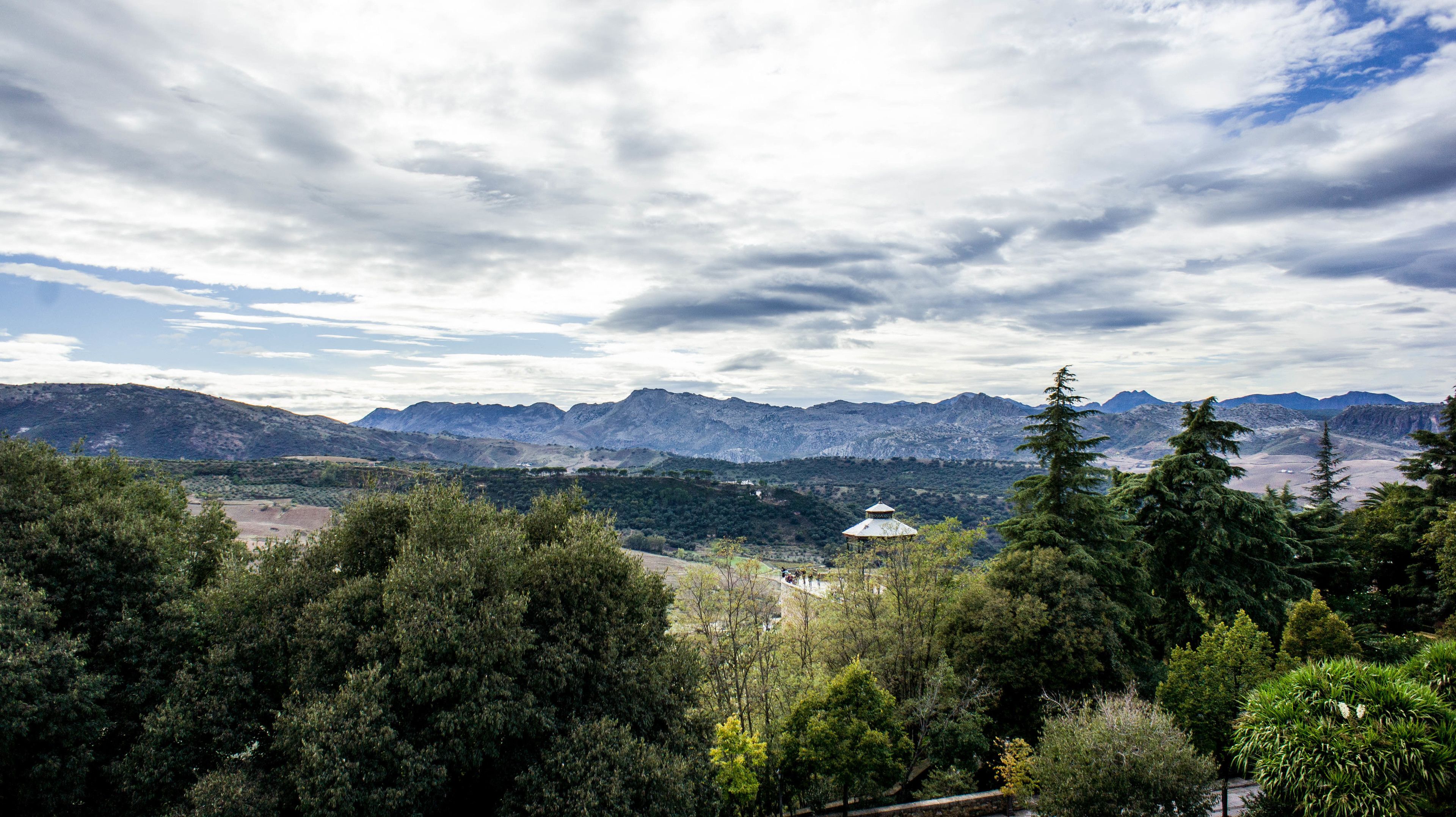 Un paysage montagneux offrant une vue sur des montagnes lointaines, avec une forêt dense au premier plan et un petit bâtiment surmonté d’un dôme.