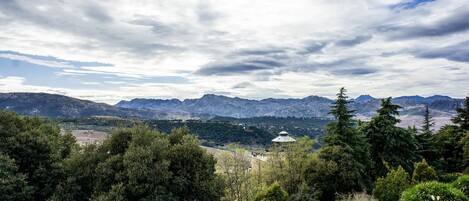 Un paysage montagneux offrant une vue sur des montagnes lointaines, avec une forêt dense au premier plan et un petit bâtiment surmonté d’un dôme.