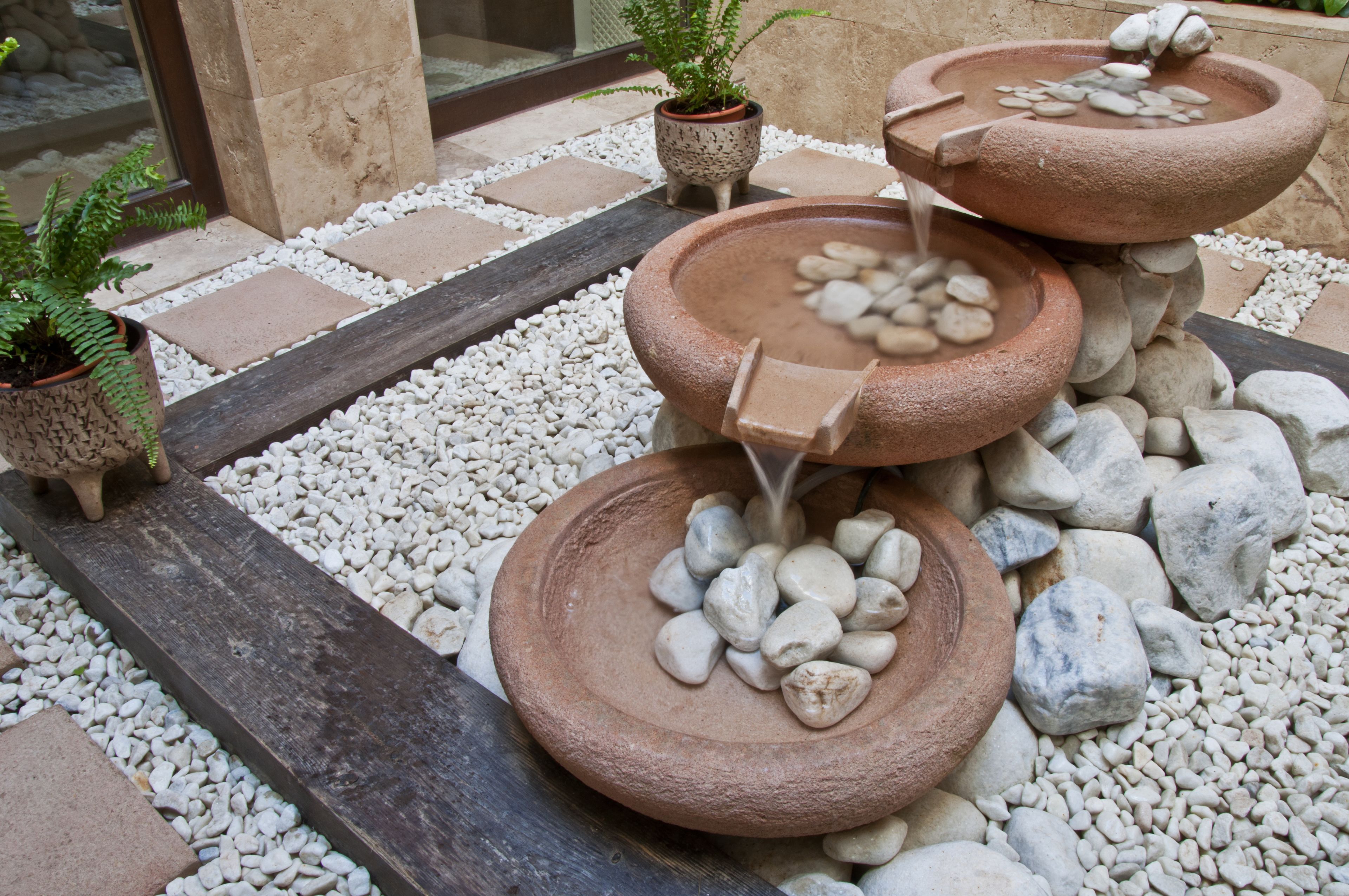 A garden with three stone water features surrounded by white pebbles and a wooden pathway.