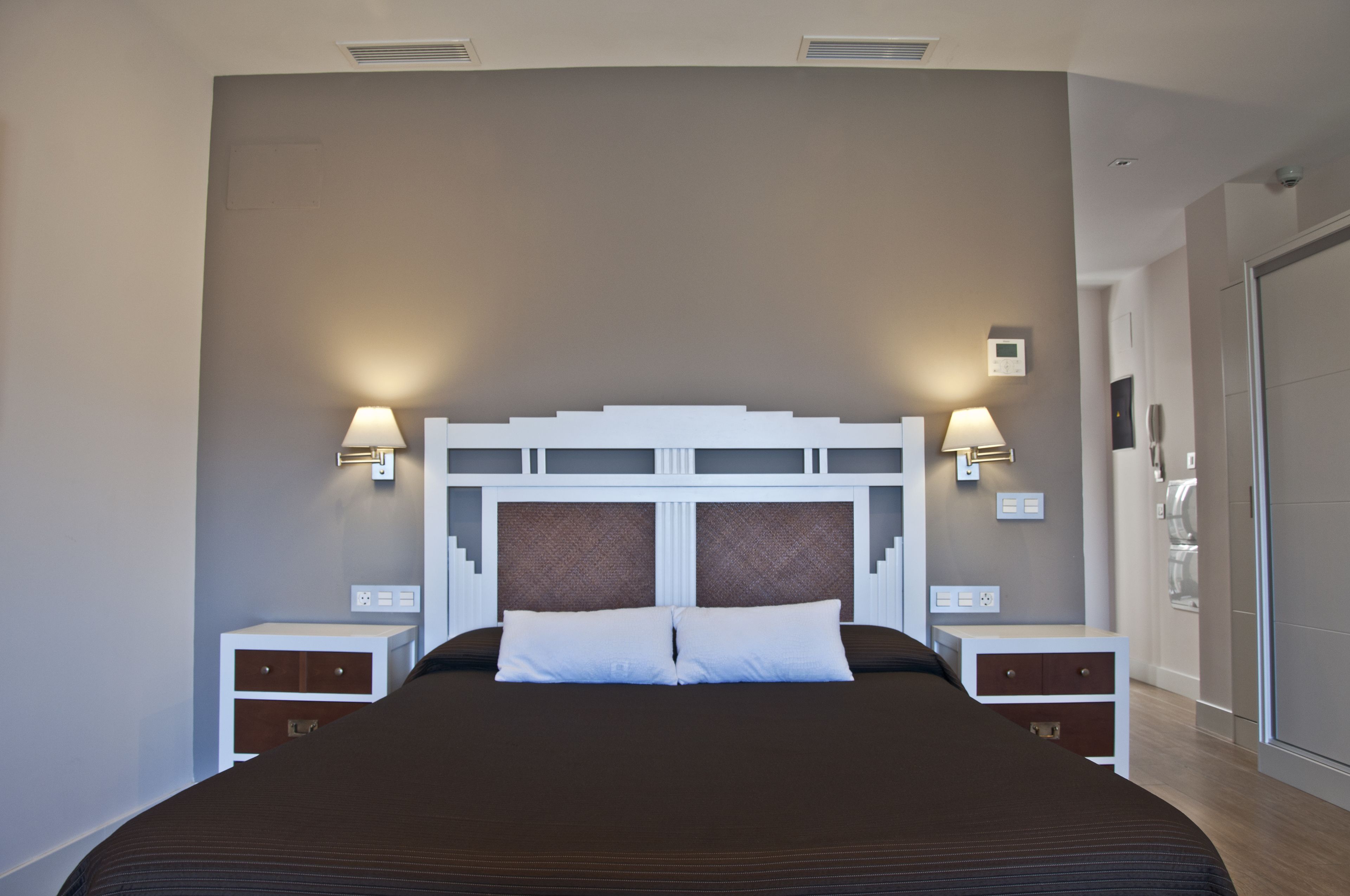 A modern hotel room with a large bed, two bedside tables, and wall-mounted lamps.