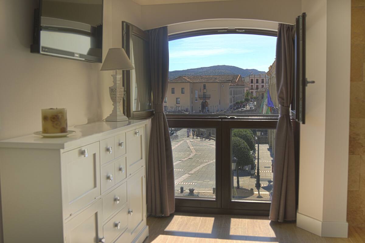 A room with a large window, a white dresser, and a lamp.