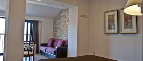 Habitación de hotel con cama, sofá, sillón y una mesita. Hay una ventana con cortinas y una pared con textura.