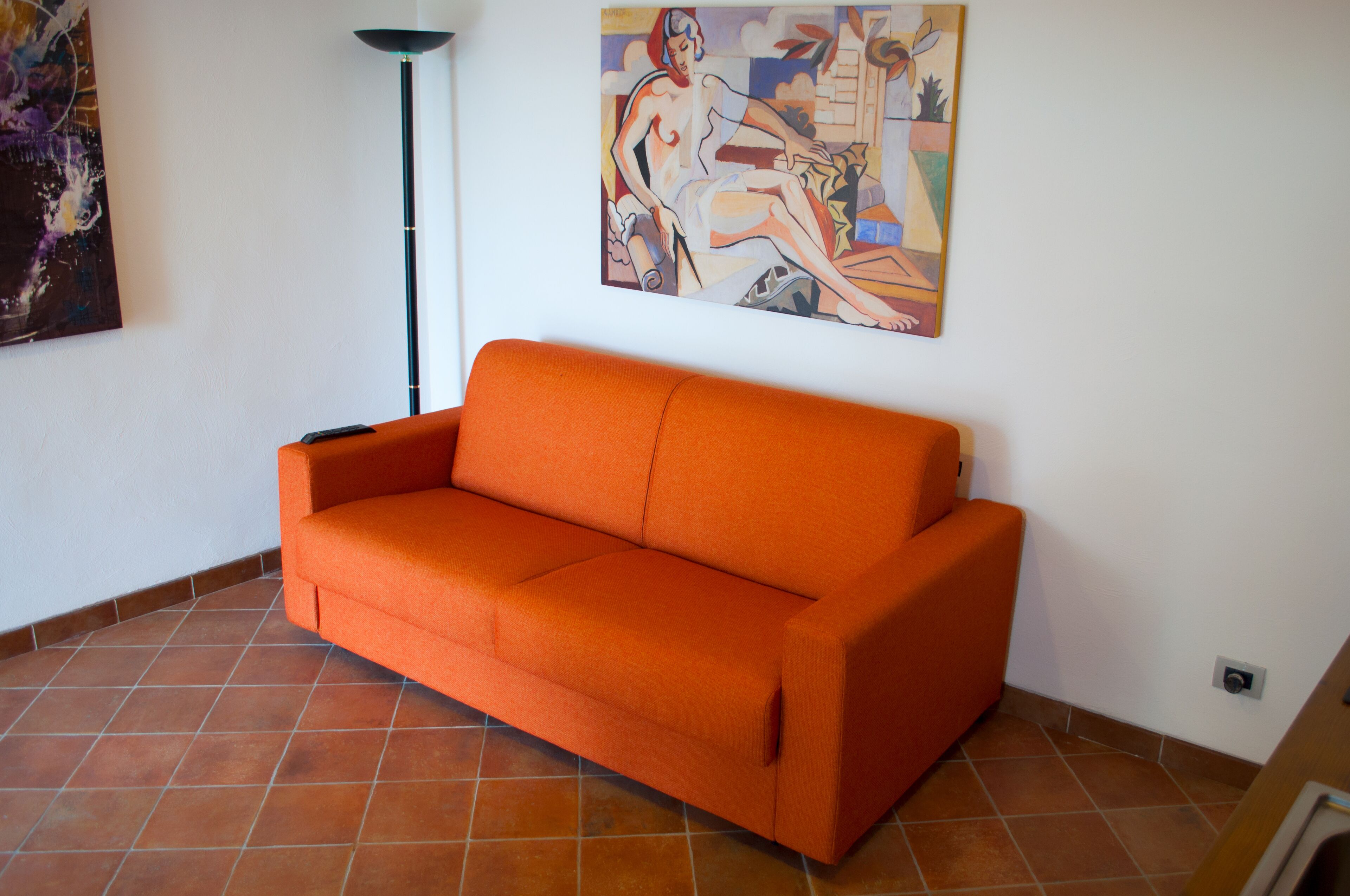 Une pièce avec un canapé orange, un lampadaire et un tableau accroché au mur.
