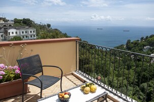 Un balcón con una silla, una mesa con frutas y vista al mar.
