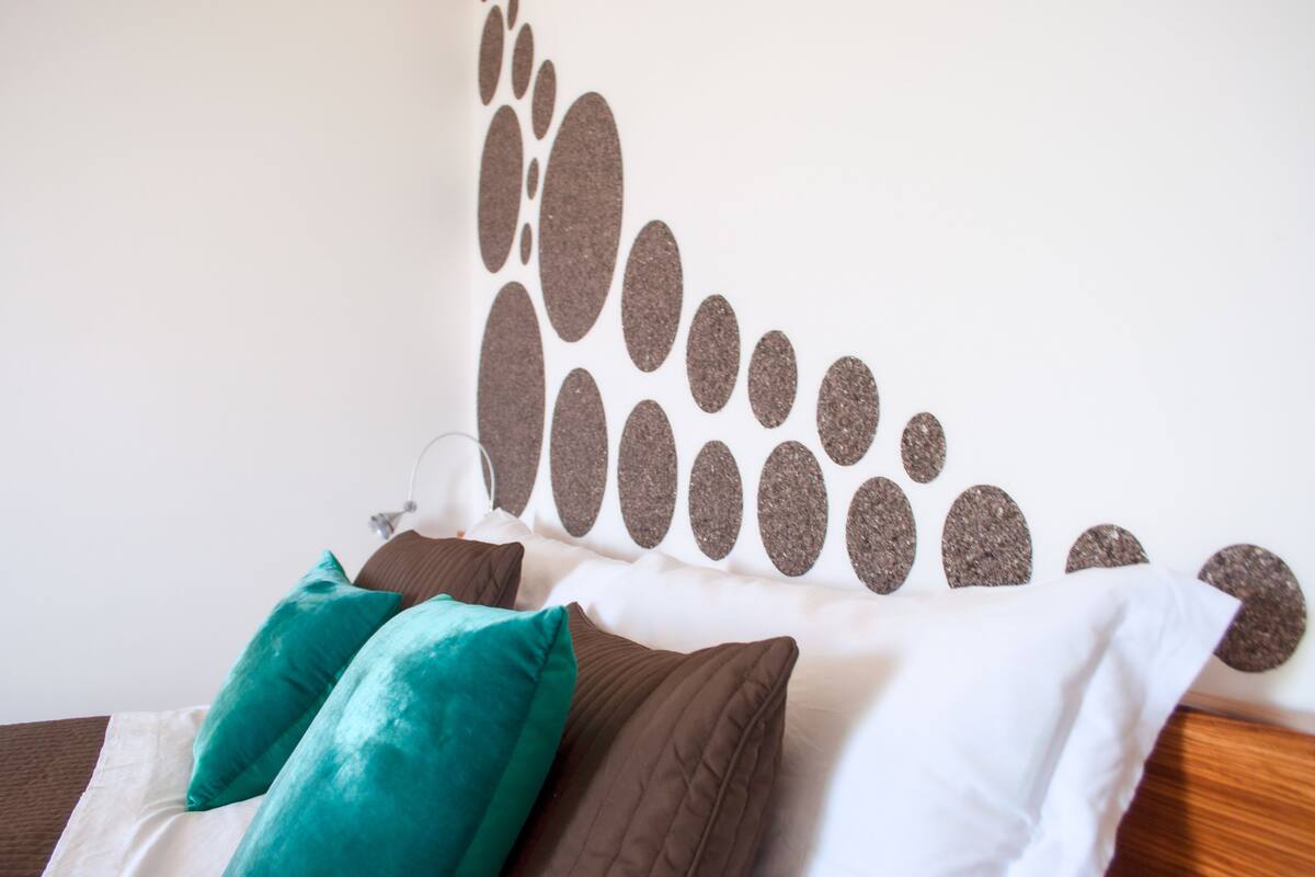 A bed with a white headboard, teal and brown pillows, and a wall with a textured, oval pattern.