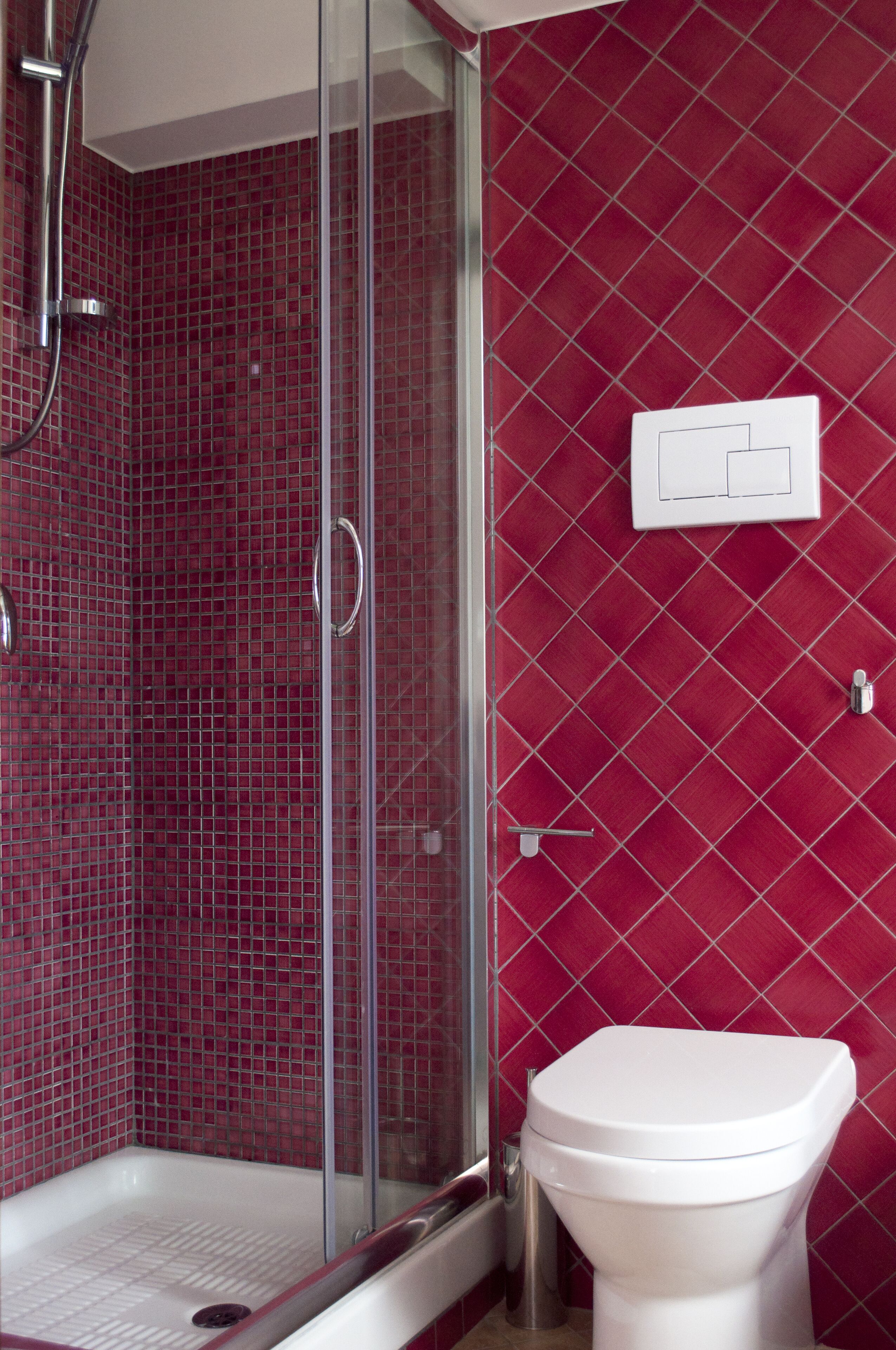 Ein Badezimmer mit einer gläsernen Duschkabine, einer weißen Toilette und einer roten Fliesenwand.