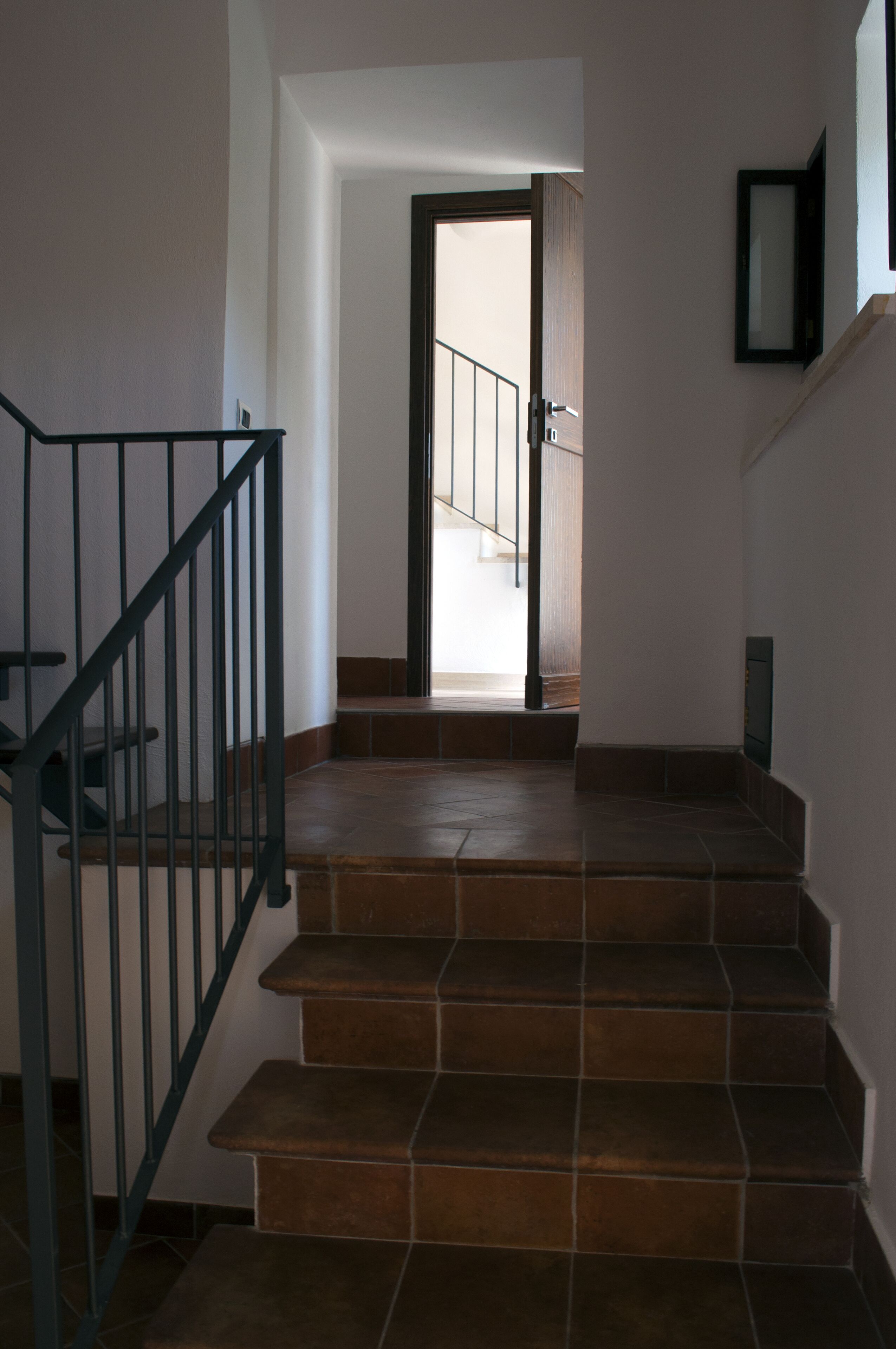 Un escalier avec une rampe métallique menant à une porte ouverte.