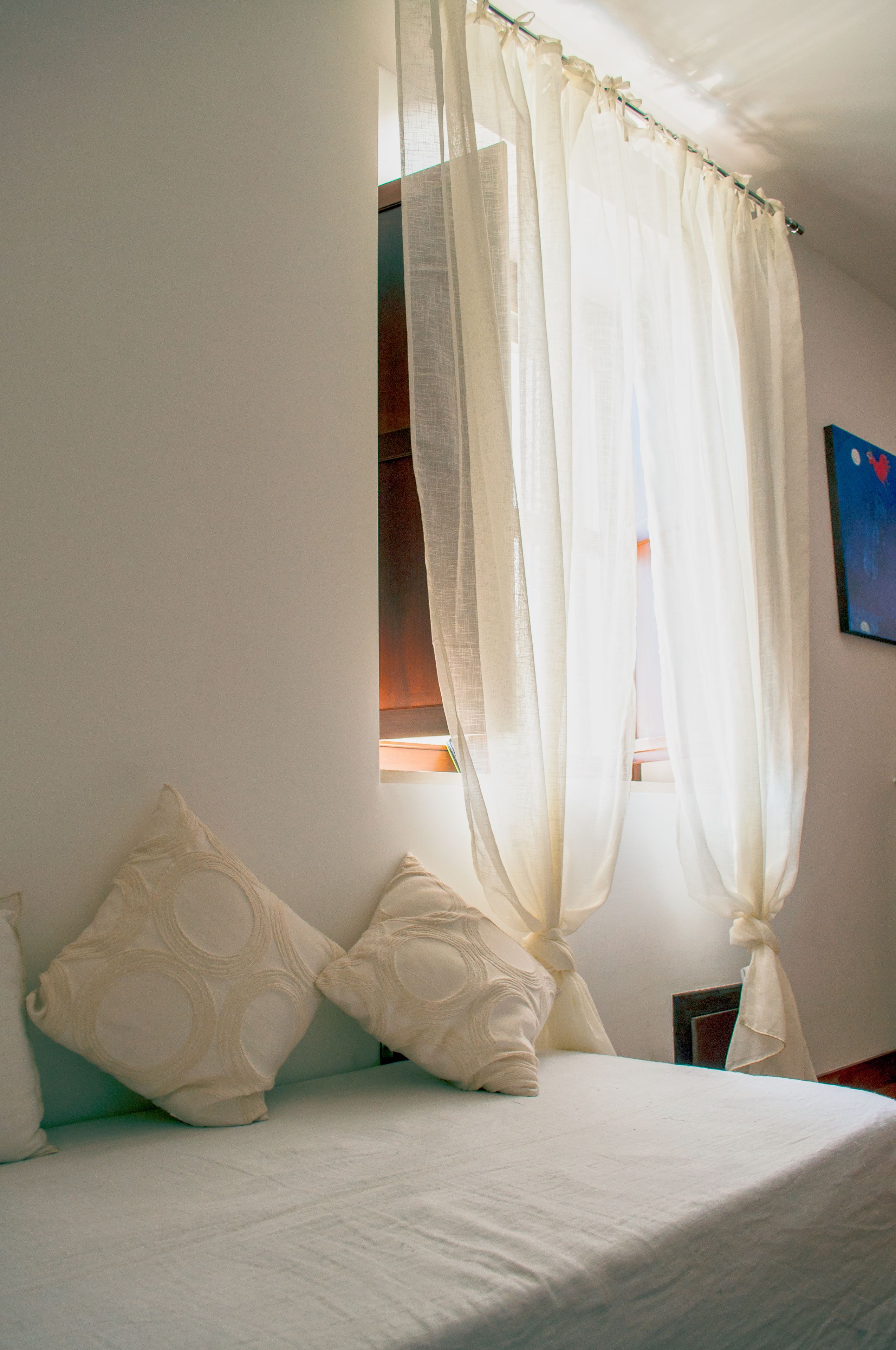 A bedroom with a bed, white curtains, and a window with a view.