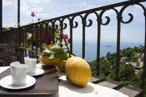 A balcony with a table set for two, a large yellow fruit, and a view of the sea.