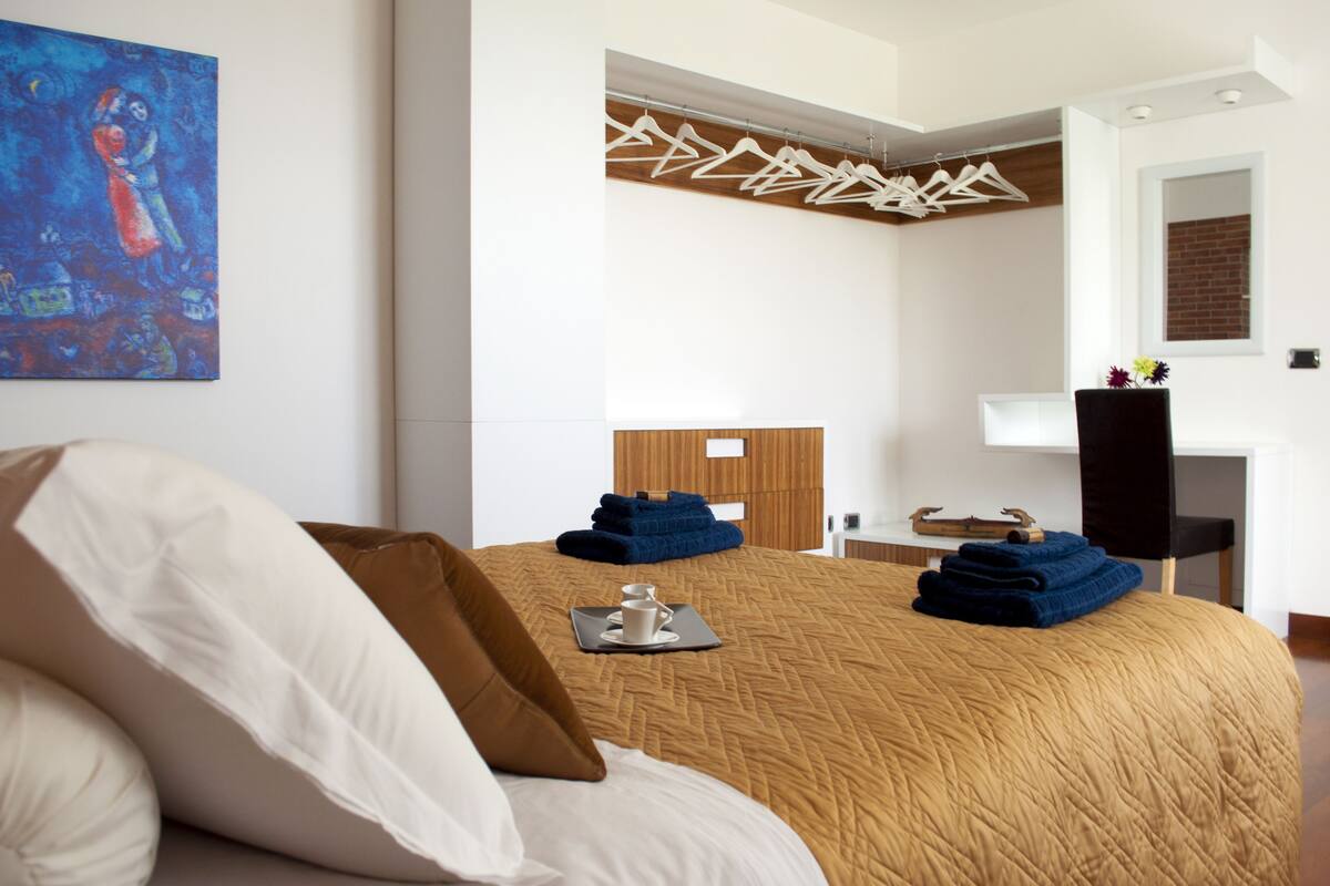A hotel room with a large bed, a wooden headboard, a painting on the wall, and a clothing rack.