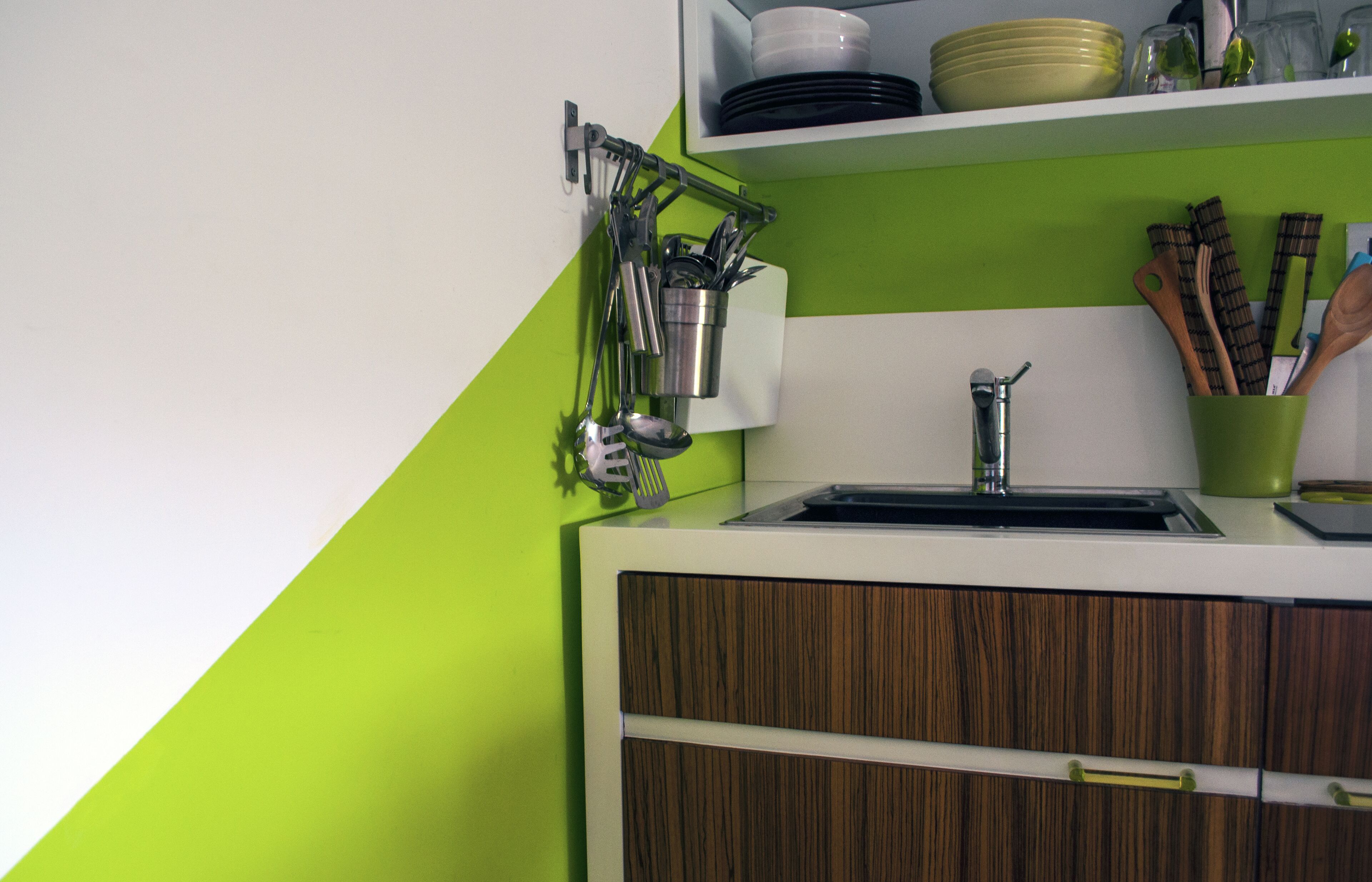 Een keuken met een groene wand, witte kasten en een roestvrijstalen spoelbak.
