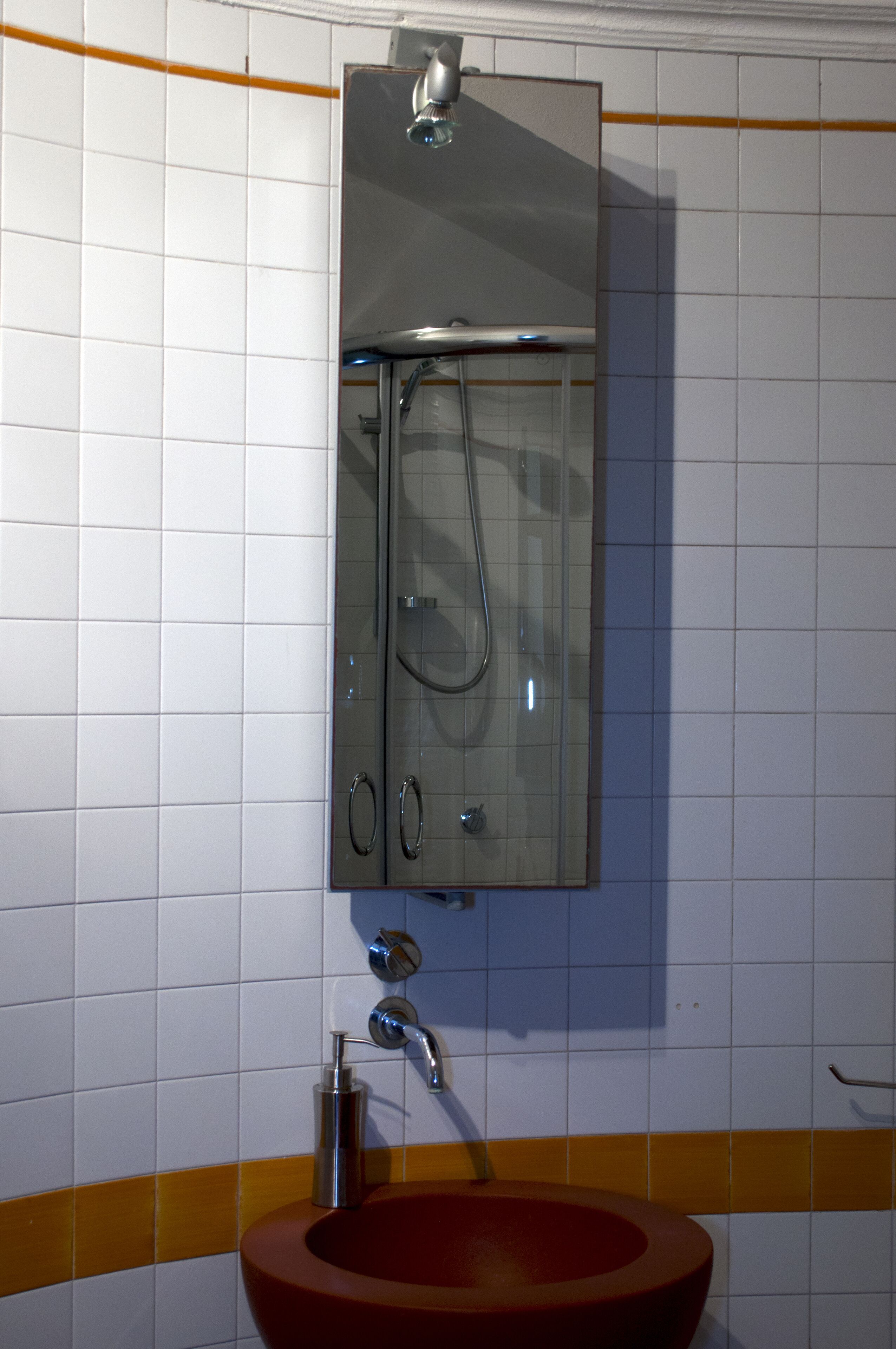 A bathroom with a glass-enclosed shower, a red sink, and white tiled walls.