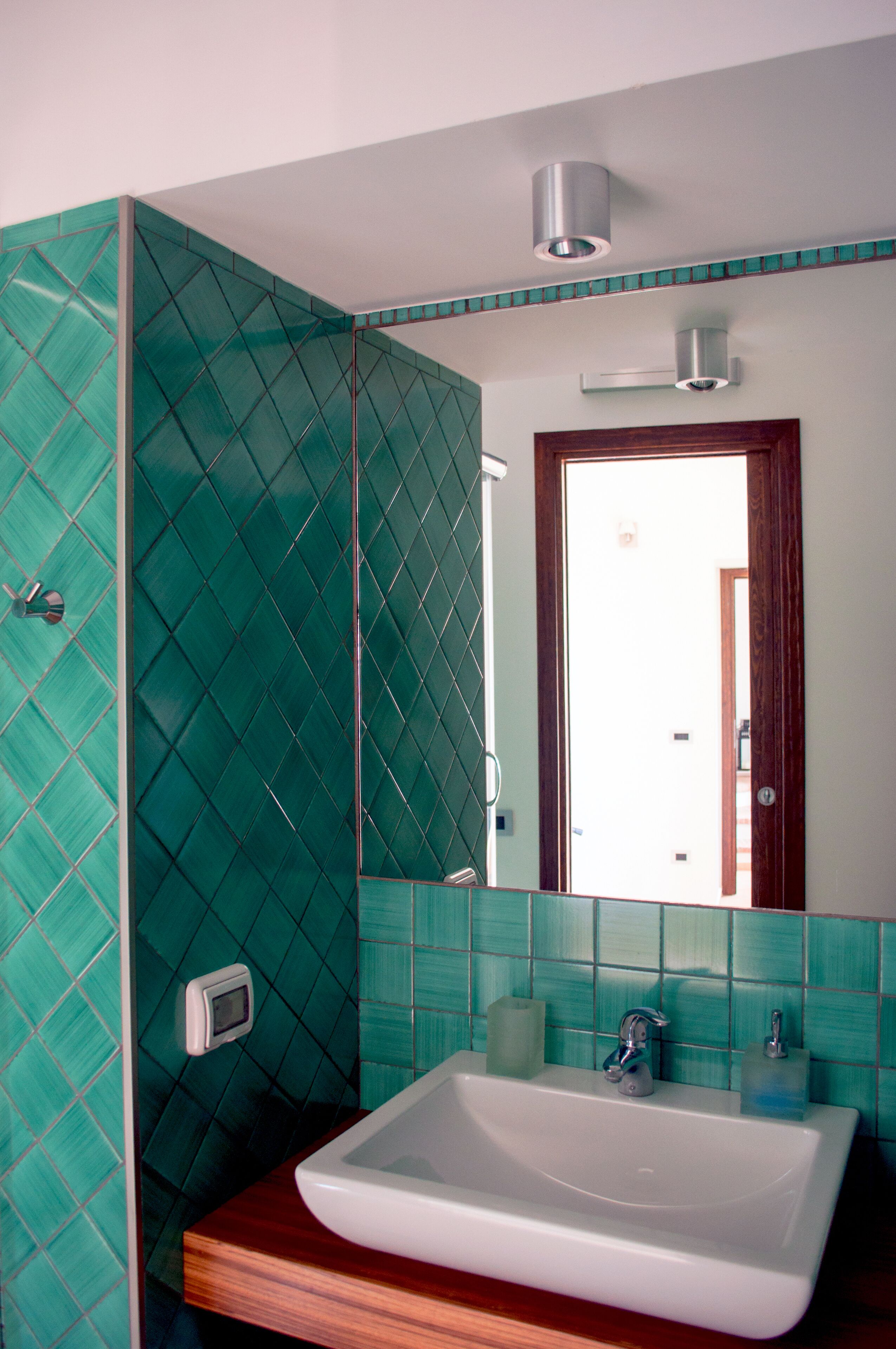 Une salle de bain avec un lavabo blanc, des murs recouverts de carreaux verts et un meuble-lavabo en bois.