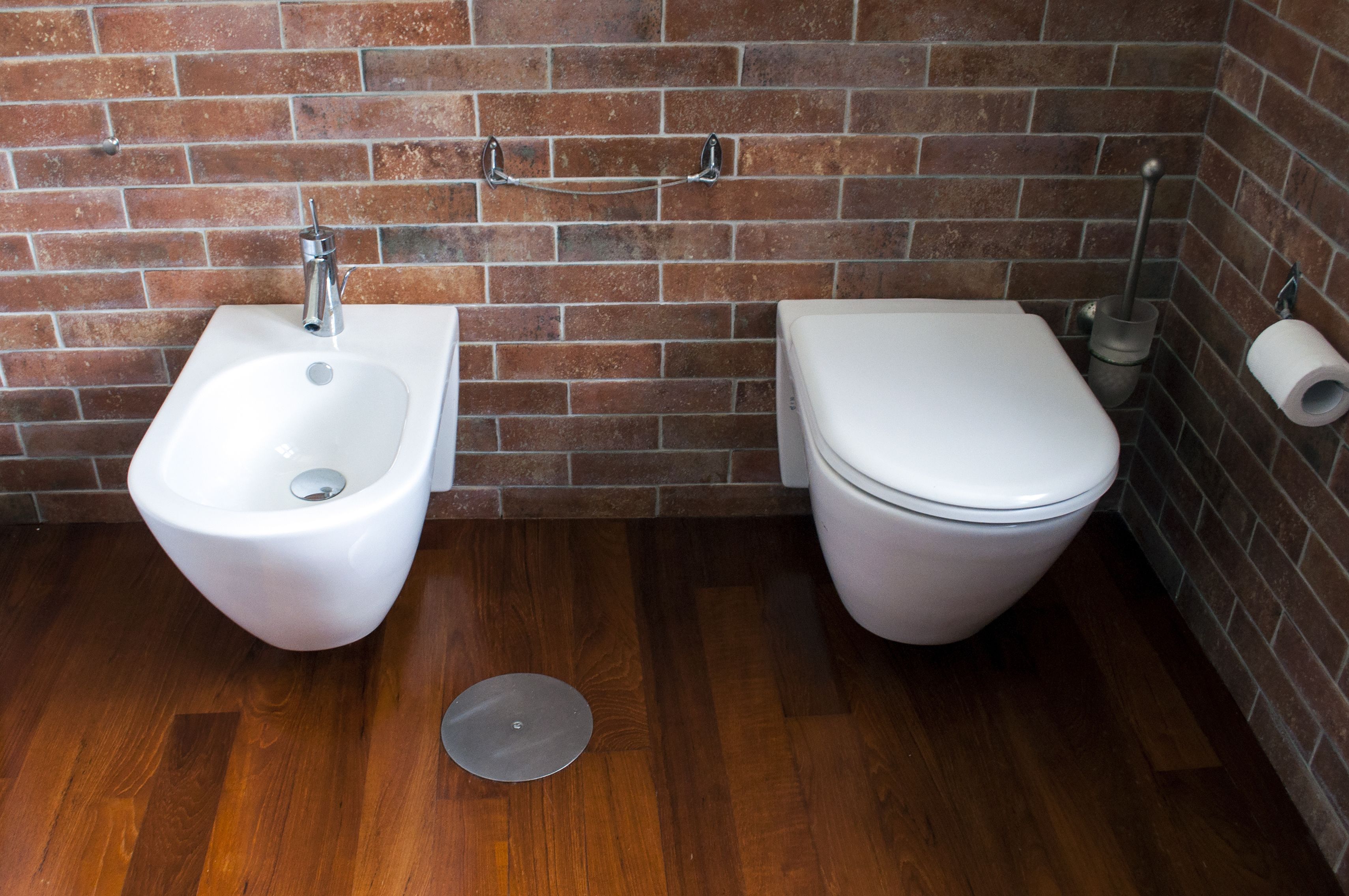 A bathroom with a bidet, toilet, and a roll of toilet paper on the wall.