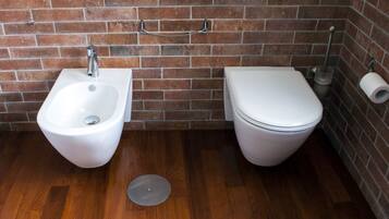 Une salle de bain équipée d’un bidet, de toilettes et d’un rouleau de papier toilette fixé au mur.