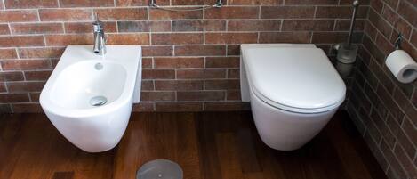 A bathroom with a bidet, toilet, and a roll of toilet paper on the wall.