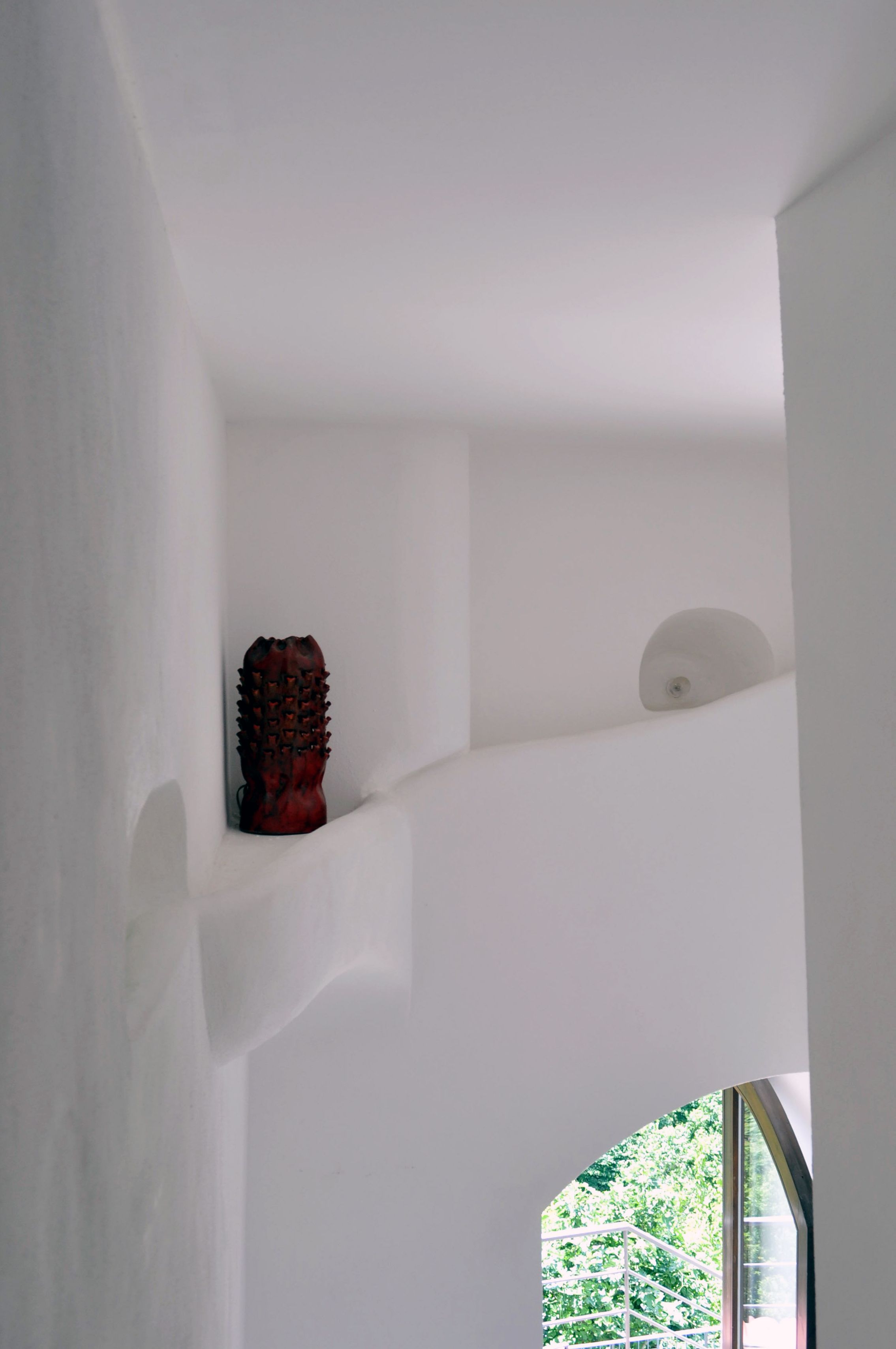 A white interior with a wooden sculpture on a shelf and a window with a view of greenery.